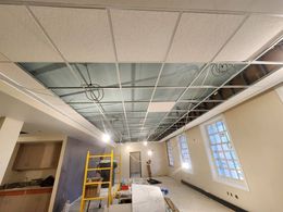 A room with a ceiling that is being remodeled and a ladder.