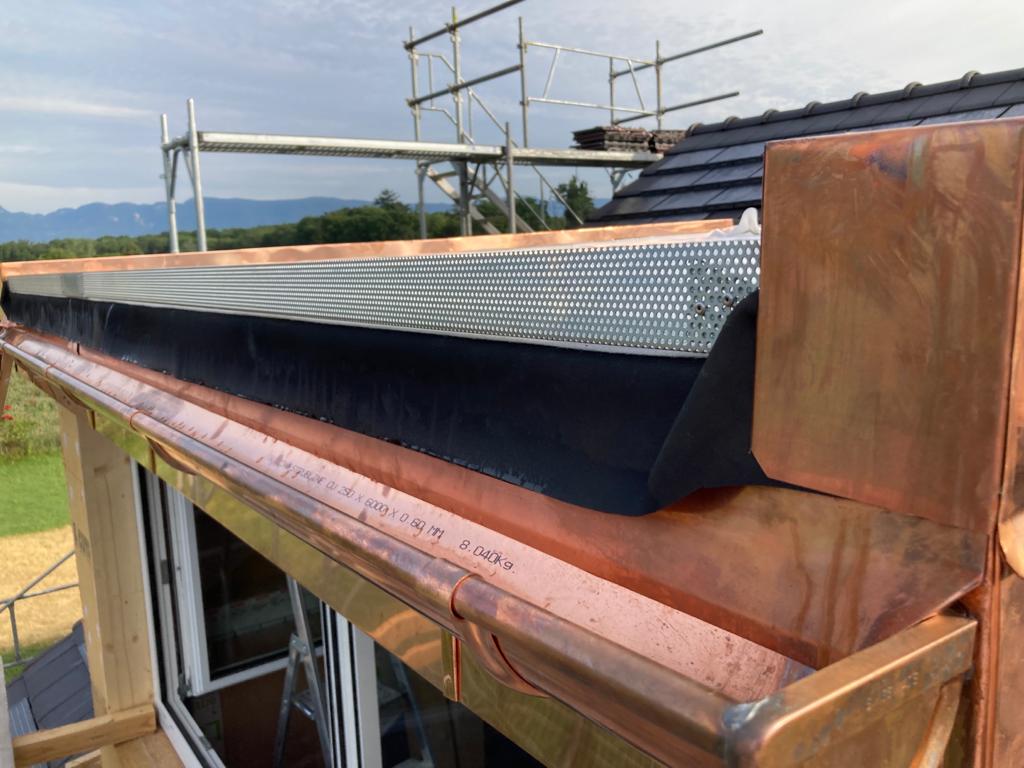 Une gouttière en cuivre est en cours d'installation sur le toit d'une maison.