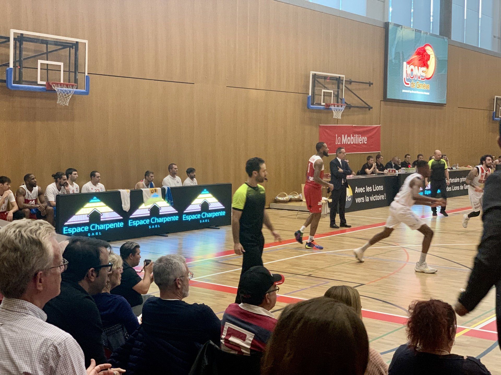 Un groupe de personnes regarde un match de basket-ball dans une salle de sport.