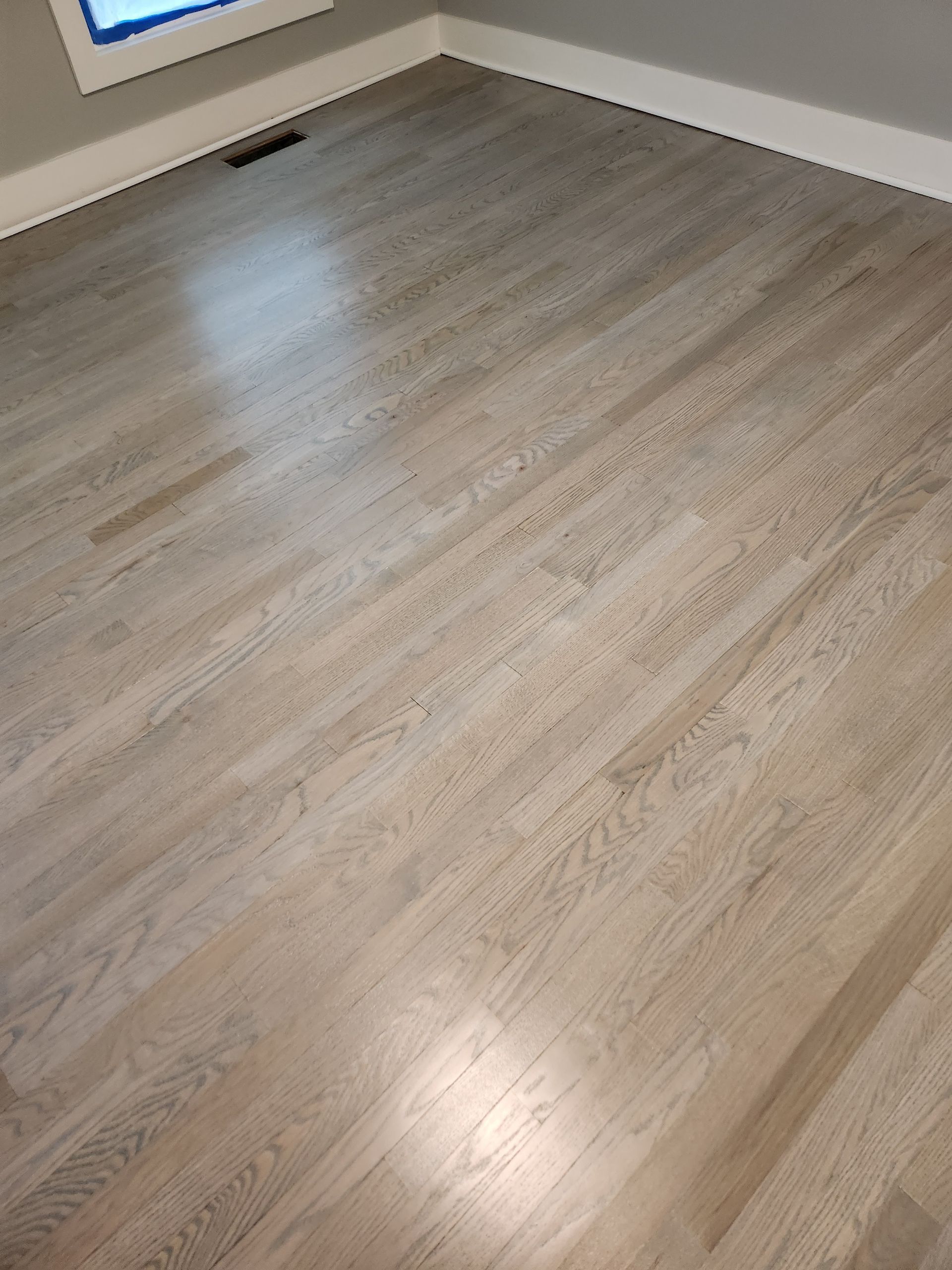 Light-colored hardwood floor in a room, with a window visible in the upper left corner.