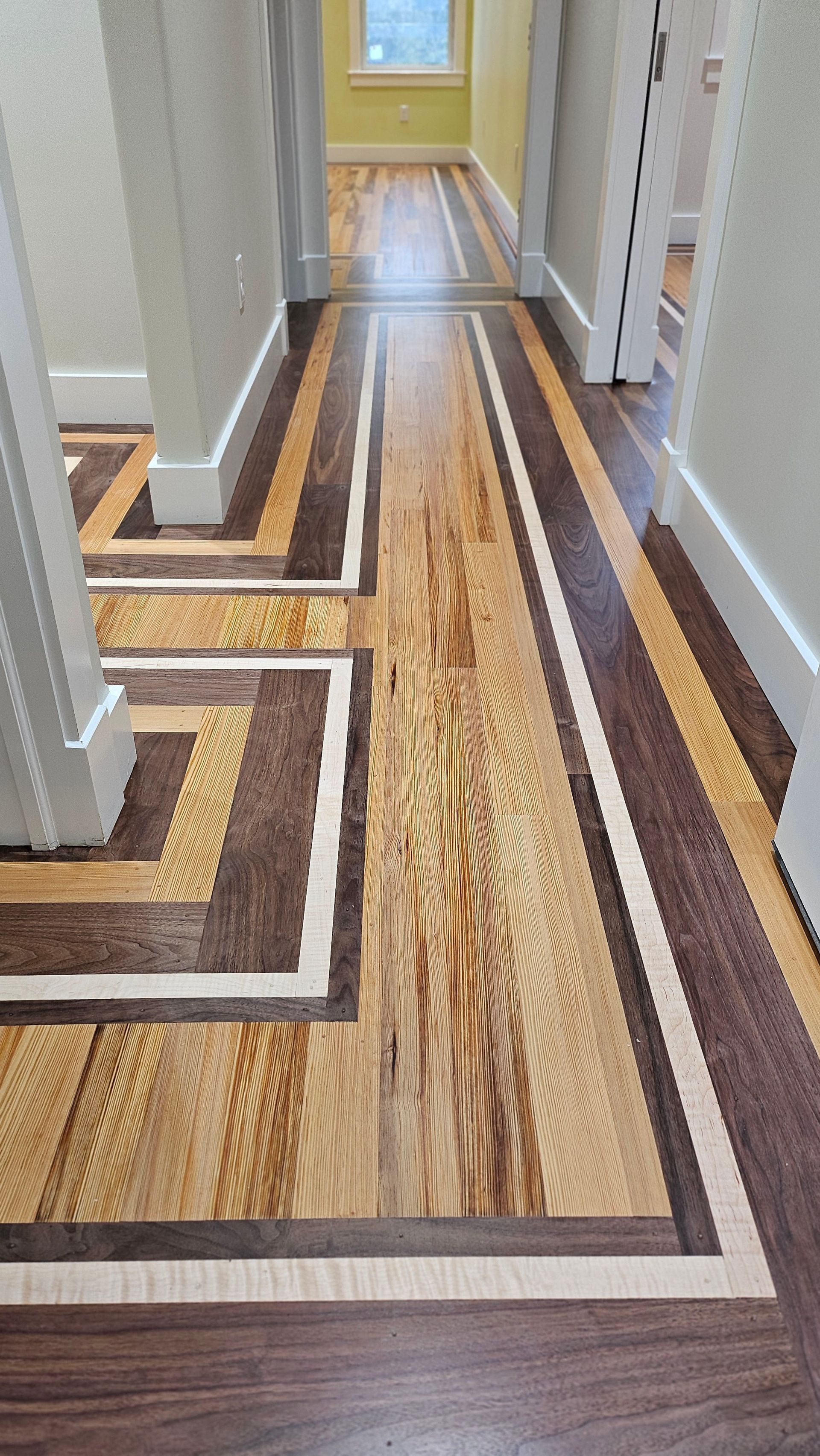 Hallway with a hardwood floor featuring a unique geometric pattern in shades of brown, beige, and cream.