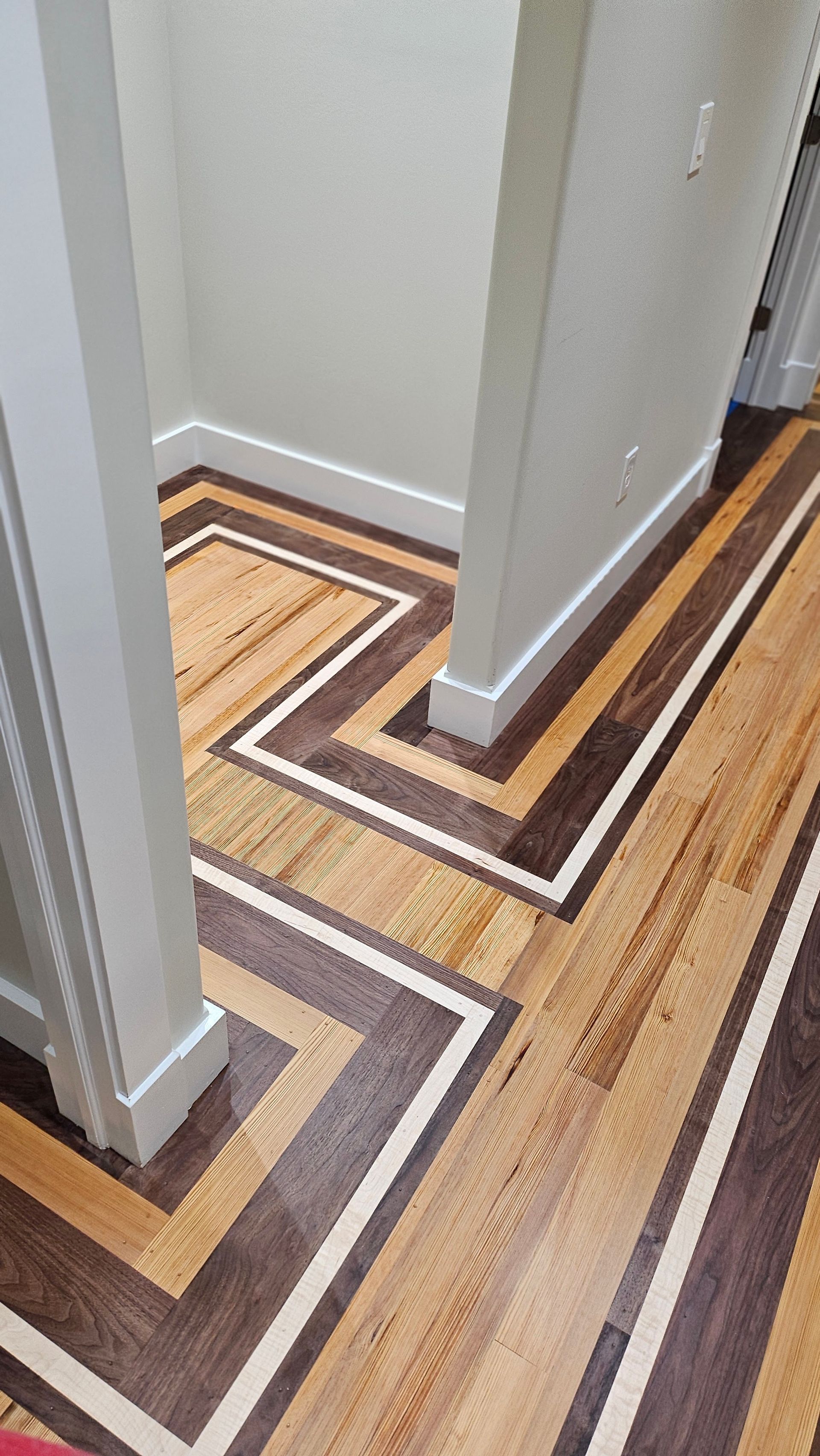 A hallway with a decorative wood floor featuring a zig-zag pattern of dark brown, light brown, and white wood planks.