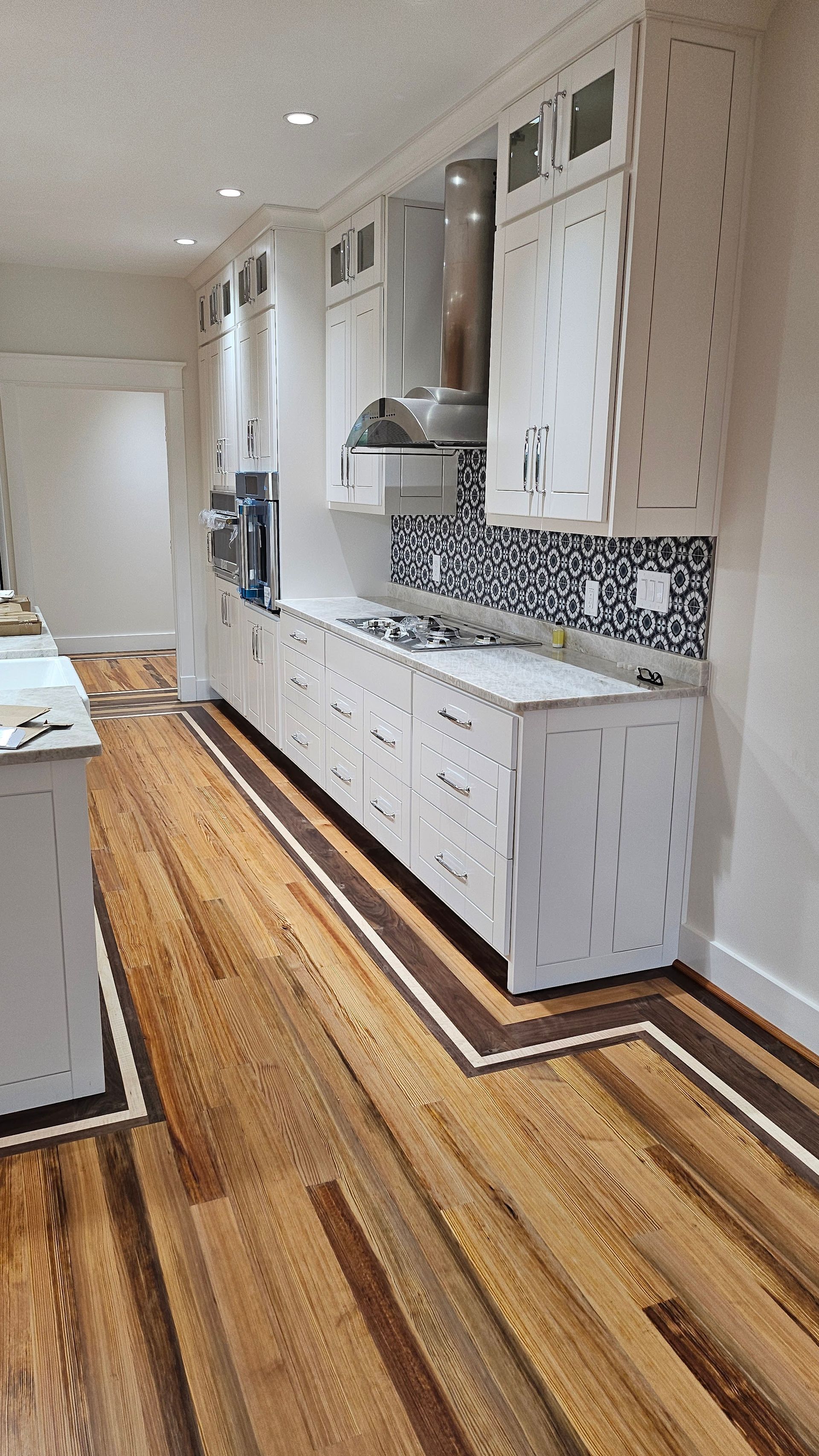 A kitchen with white cabinets, a stove and black and white tiled backsplash, set against hardwood floors with a dark border.