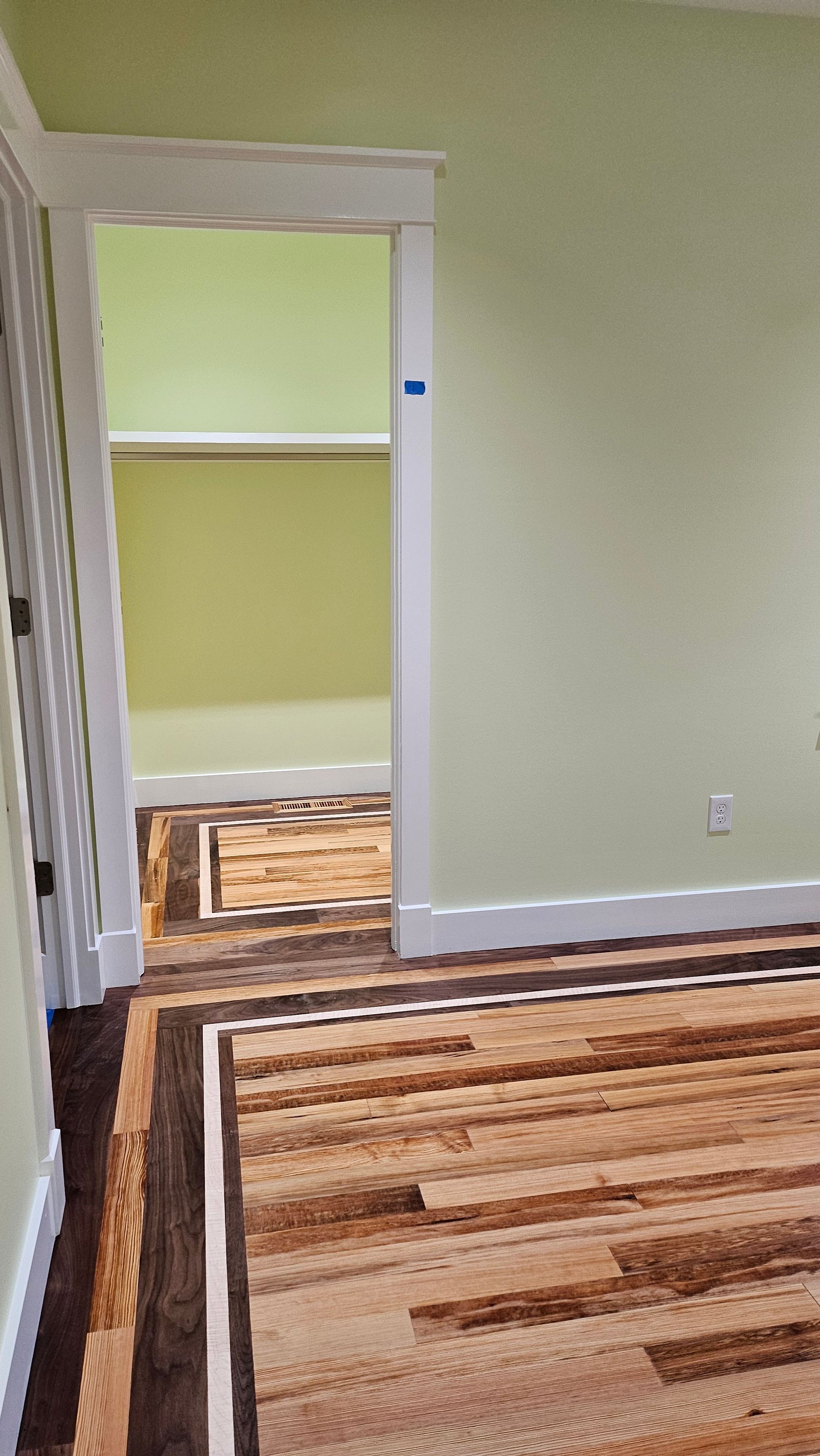 Wooden floor with a patterned border leads into a room with light green walls and an open doorway to another room.