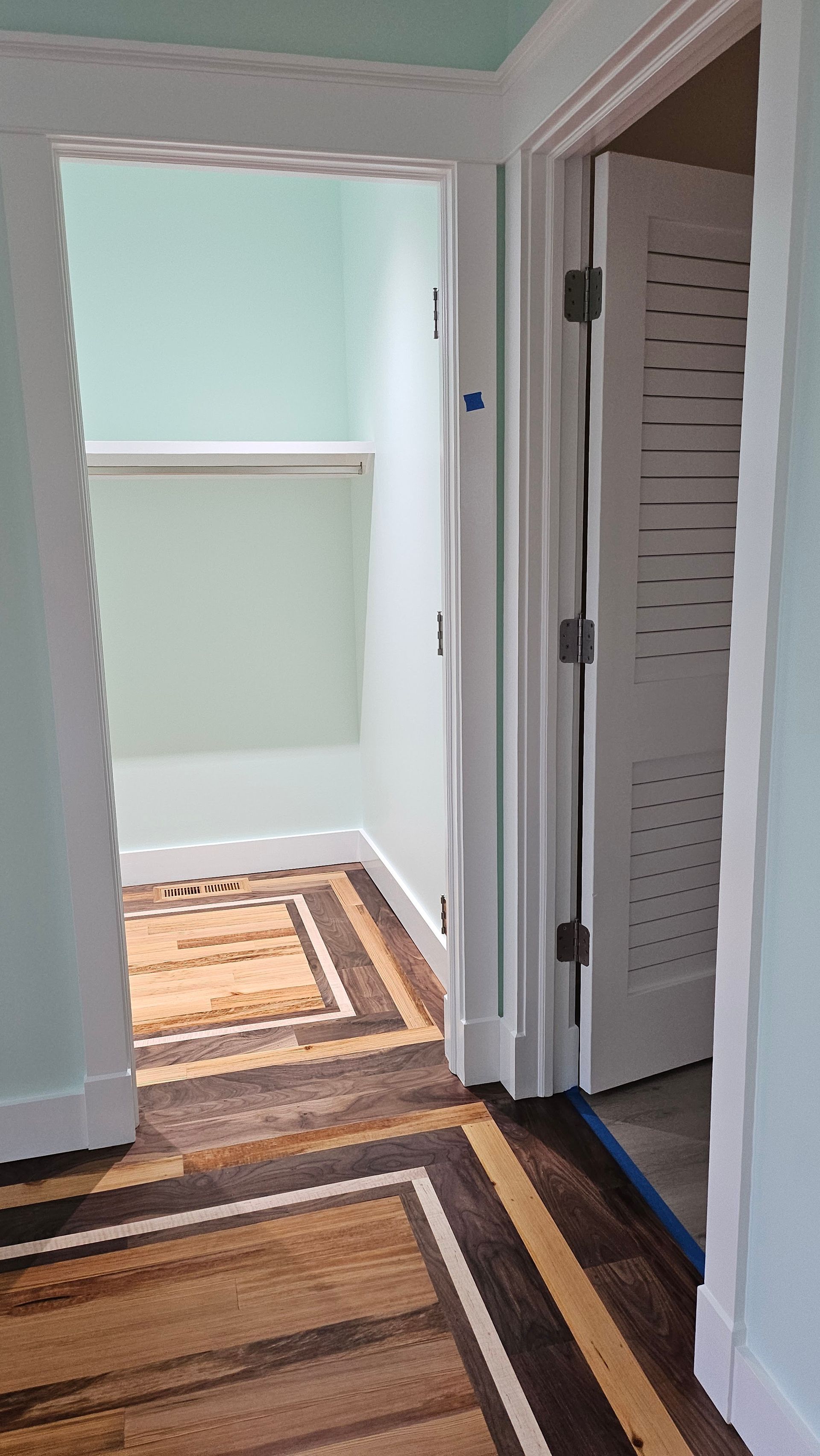 A hallway with patterned wood flooring leads to an open doorway and a closet. The walls are light teal.