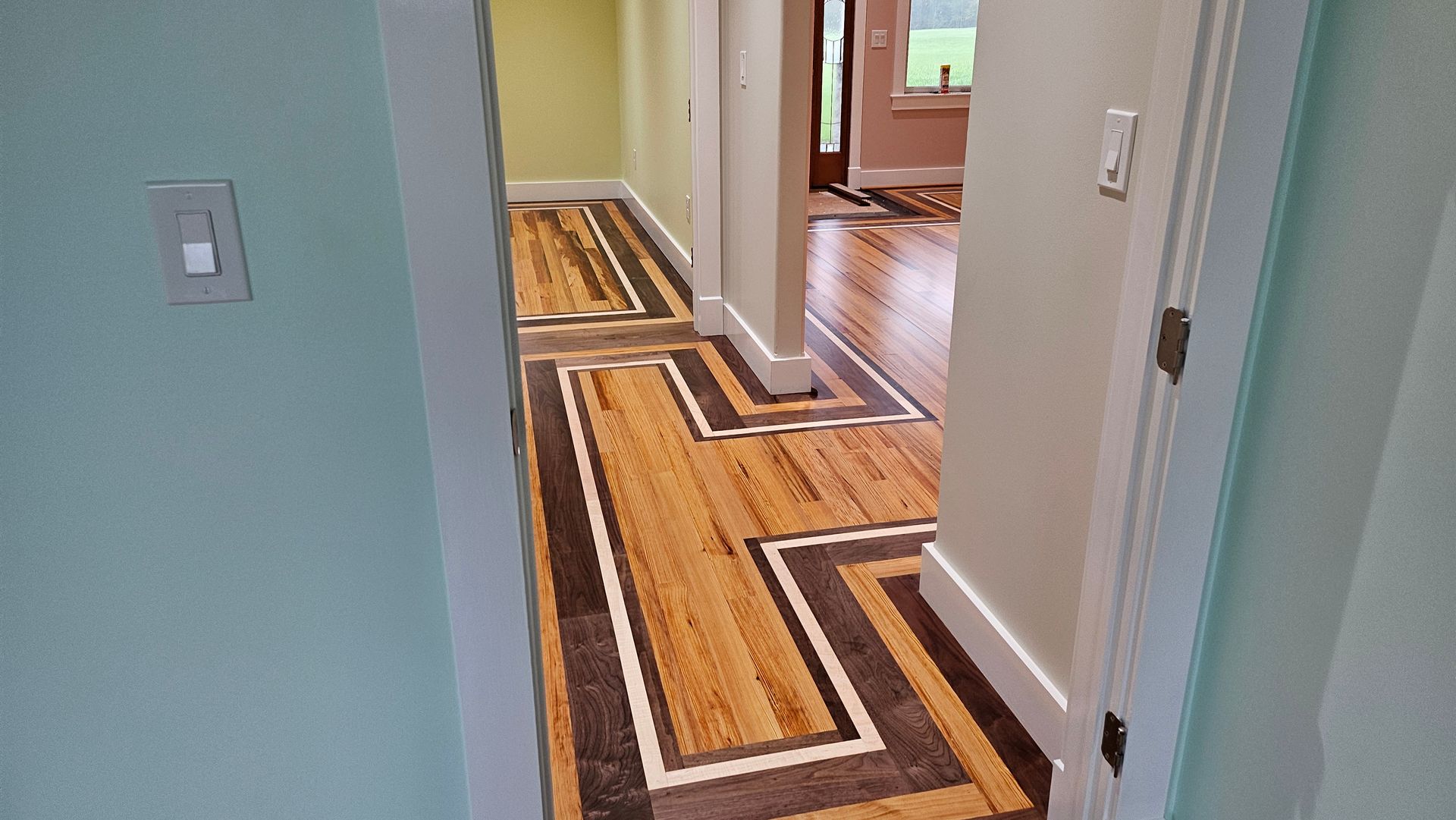 Hallway with patterned hardwood flooring framed by white walls and light green walls.