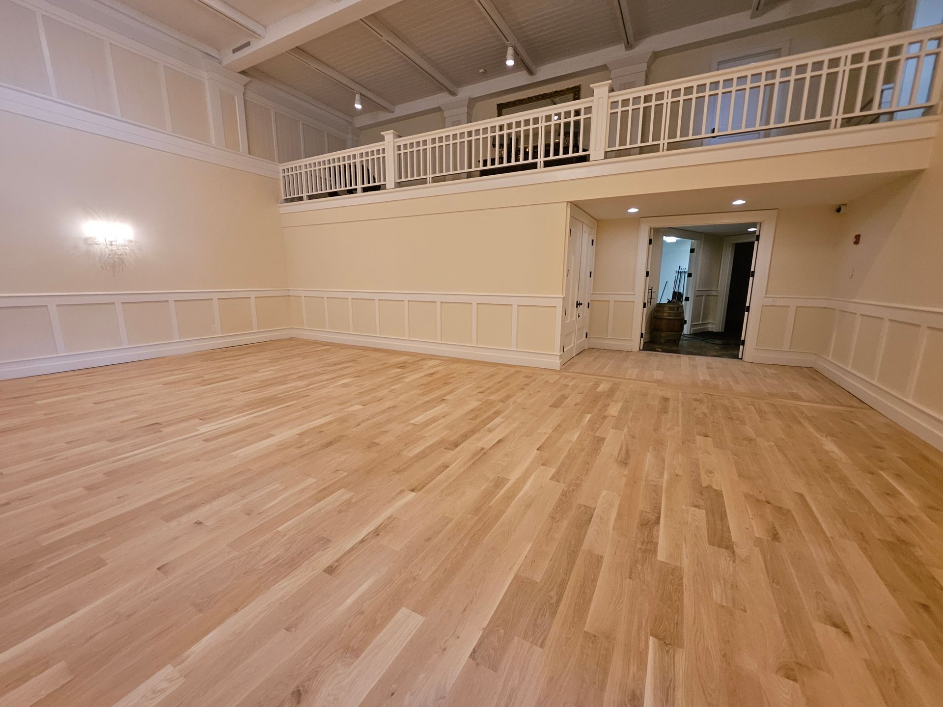 Empty room with light wood floors, white wainscoting, and a mezzanine with a white railing.
