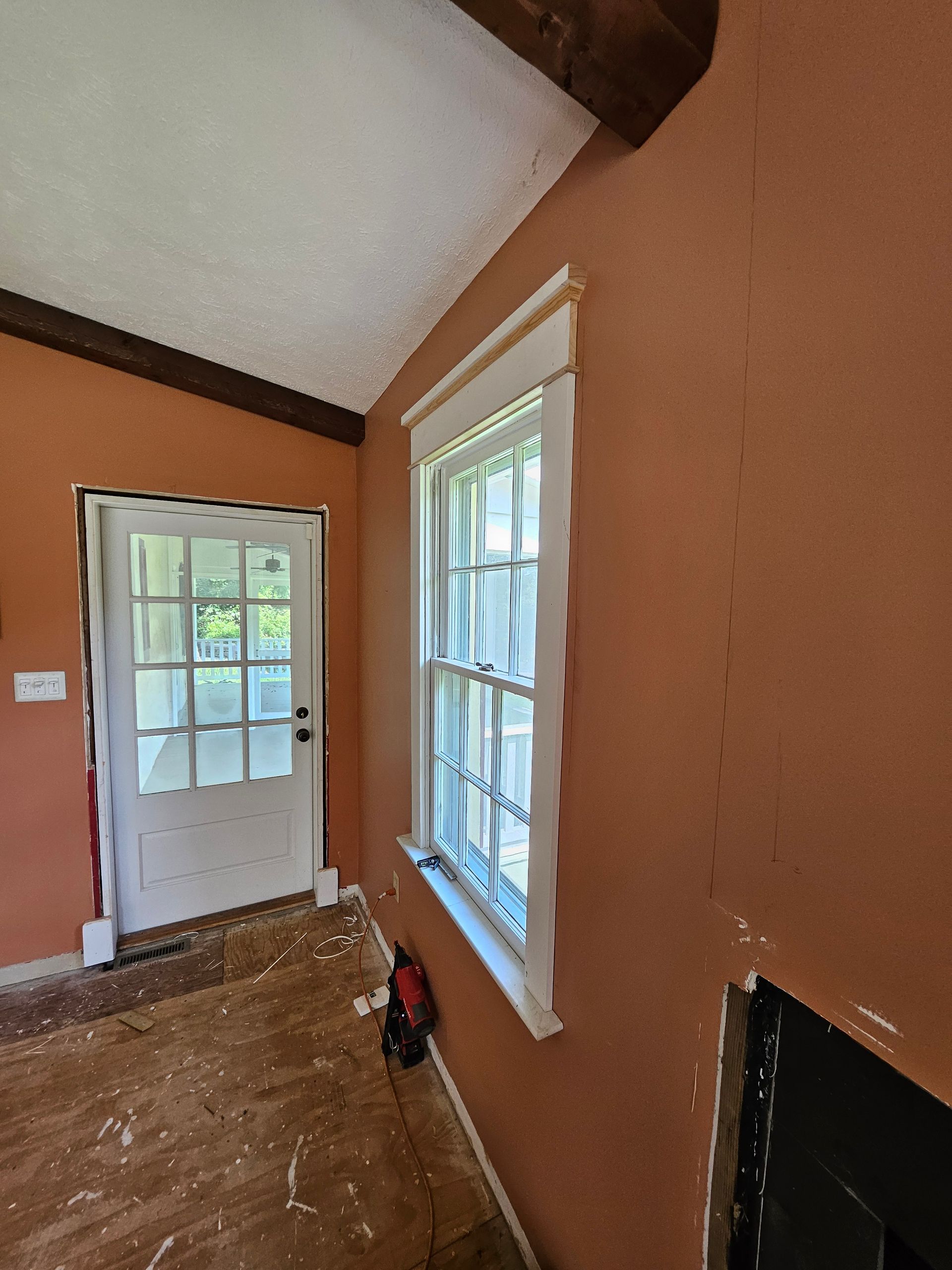 Interior view of a room with orange walls, white window and door trim. A white glass door and window are present. The room appears to be under renovation.