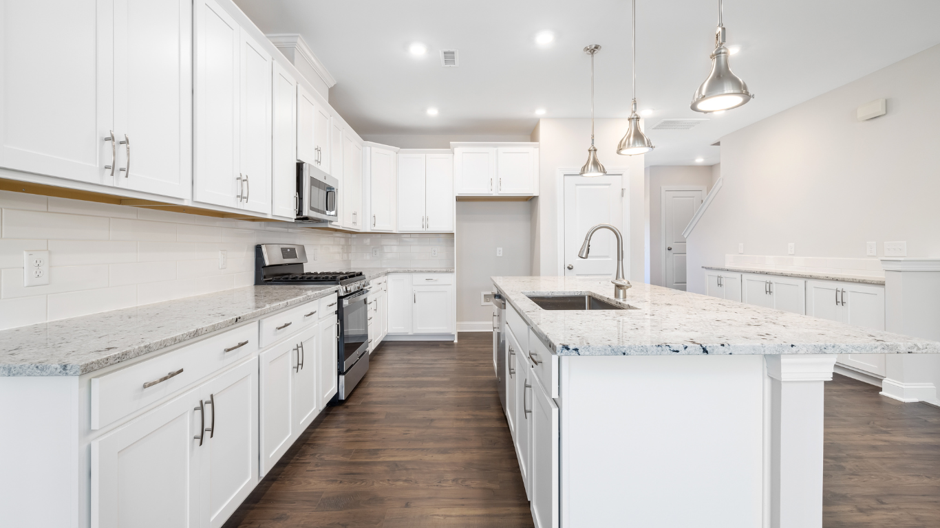 White kitchen with granite countertops, stainless steel appliances, and a large island. Dark wood floors and modern lighting.