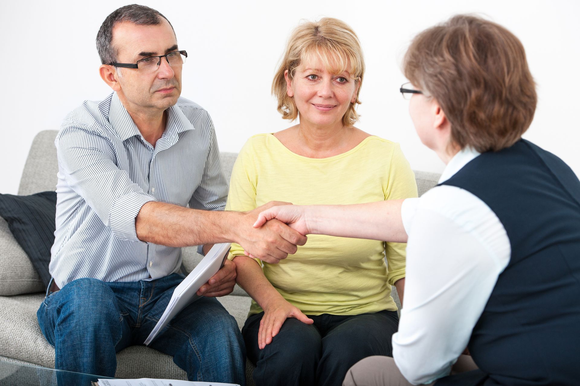 A man and woman are shaking hands with a woman while sitting on a couch.