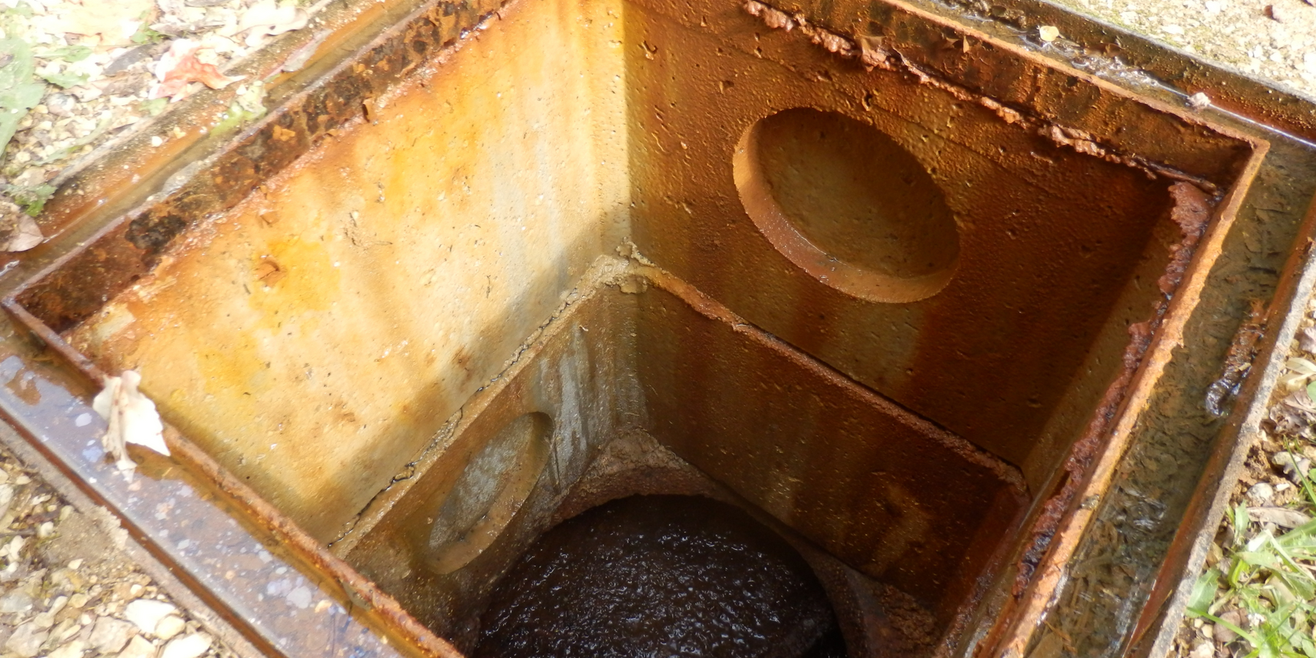 Open, rusted metal drain. The interior reveals a dark, rounded object.