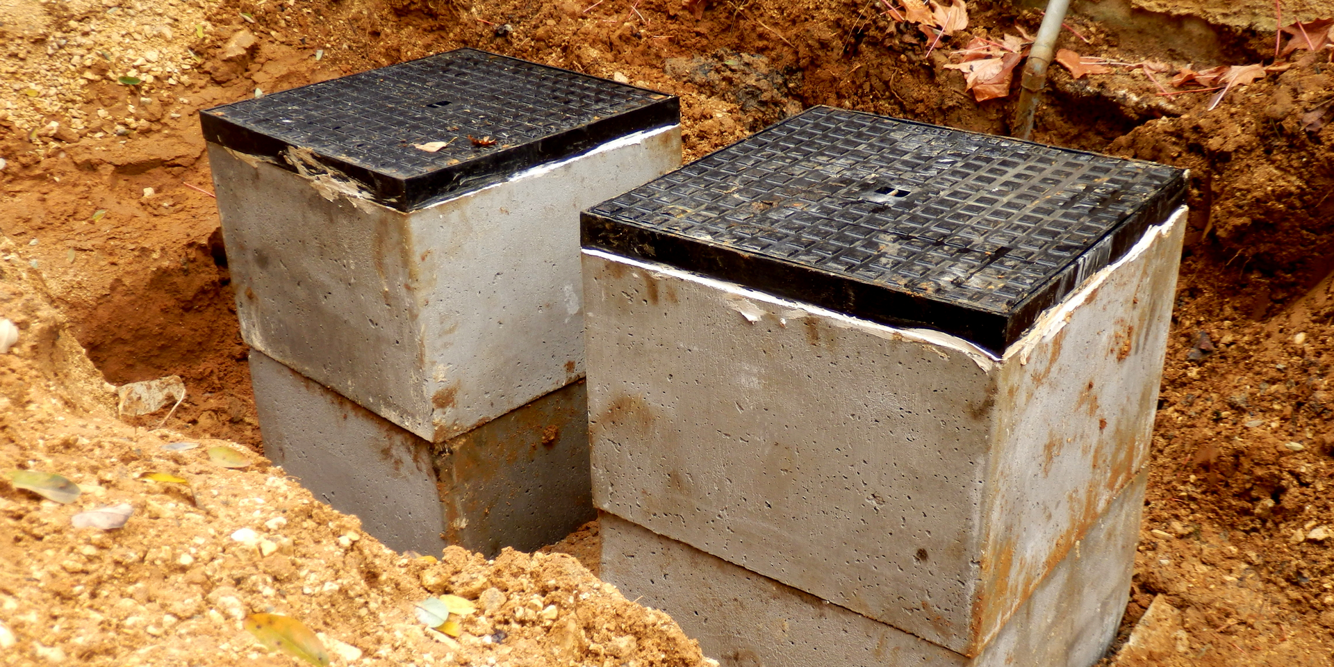Two concrete boxes with black lids, partially buried in dirt.
