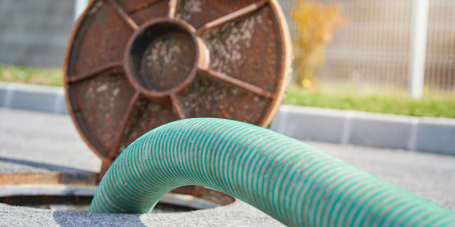 Green corrugated hose extending from a rusty manhole cover.