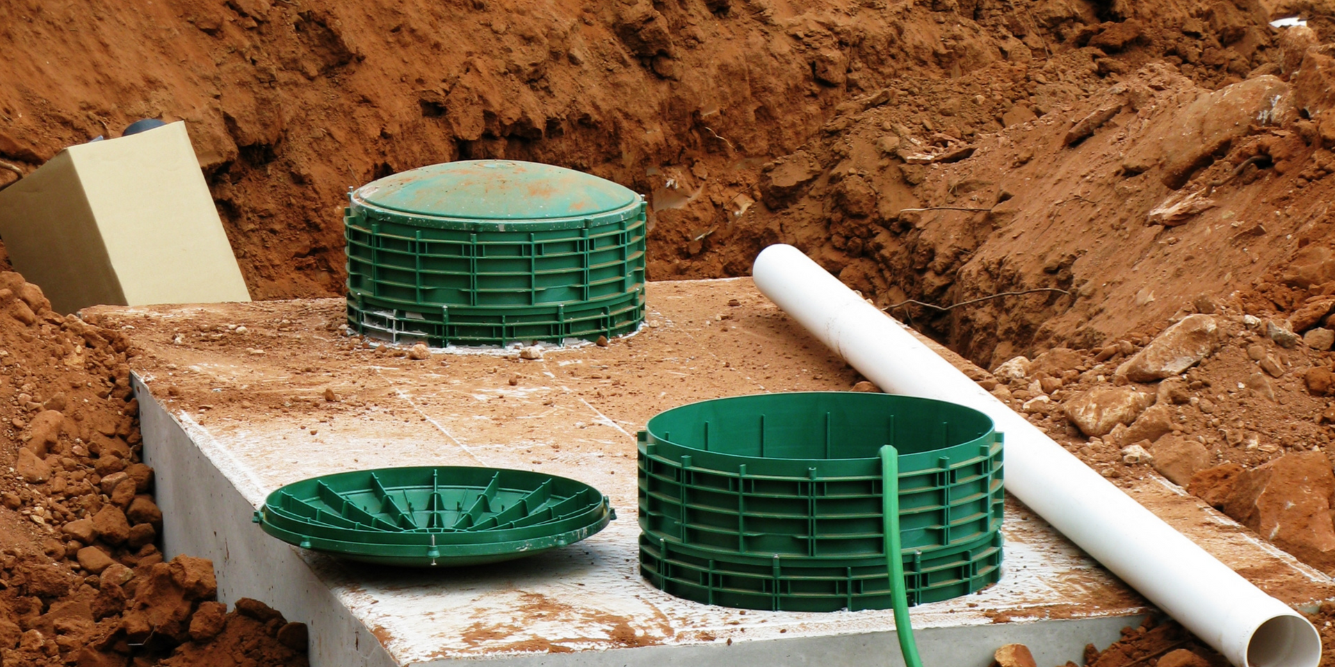 Installation of a septic tank system. Green plastic components are in a dirt trench with a white pipe.