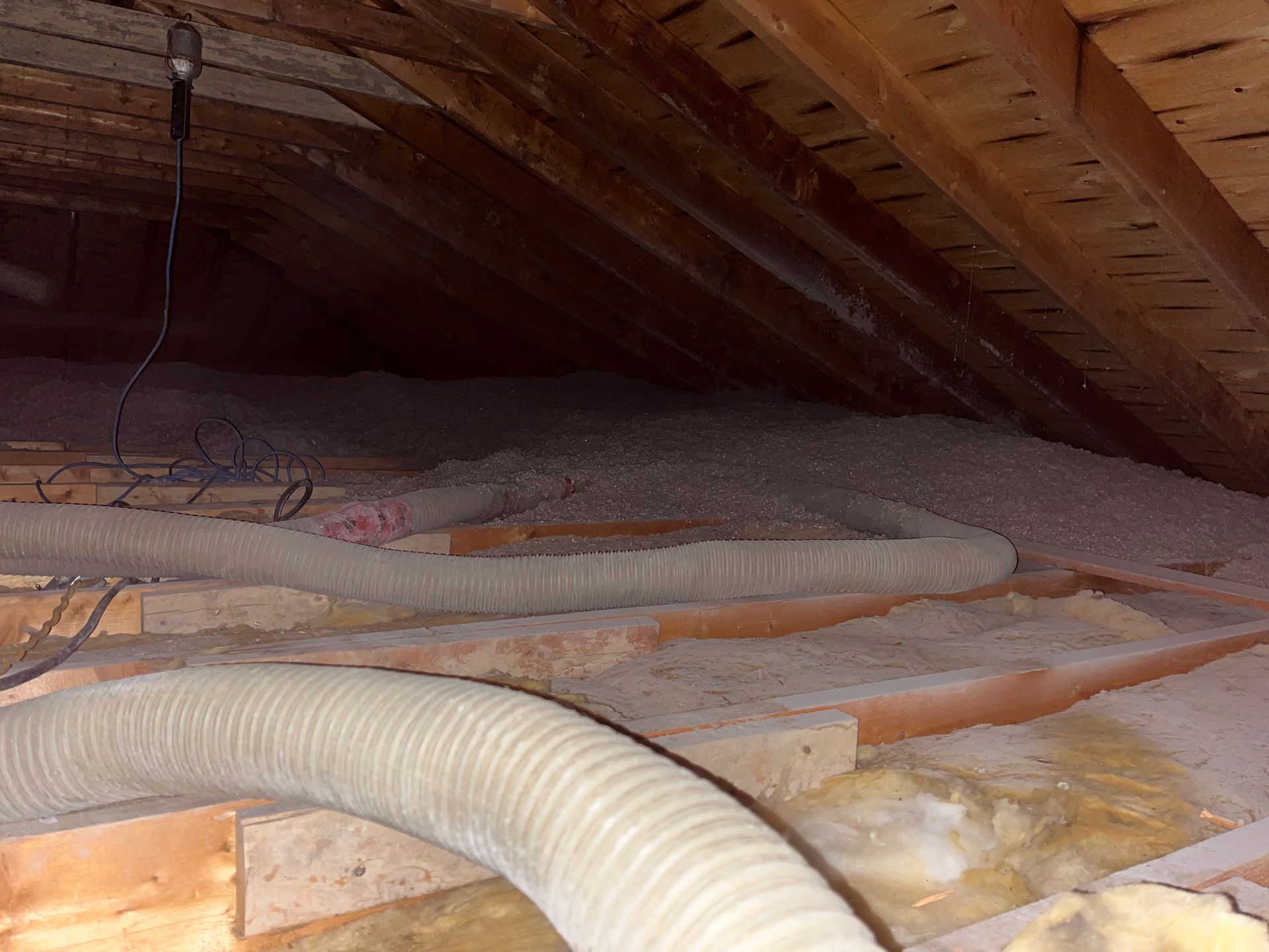 Attic interior with insulation and ductwork among wooden beams.