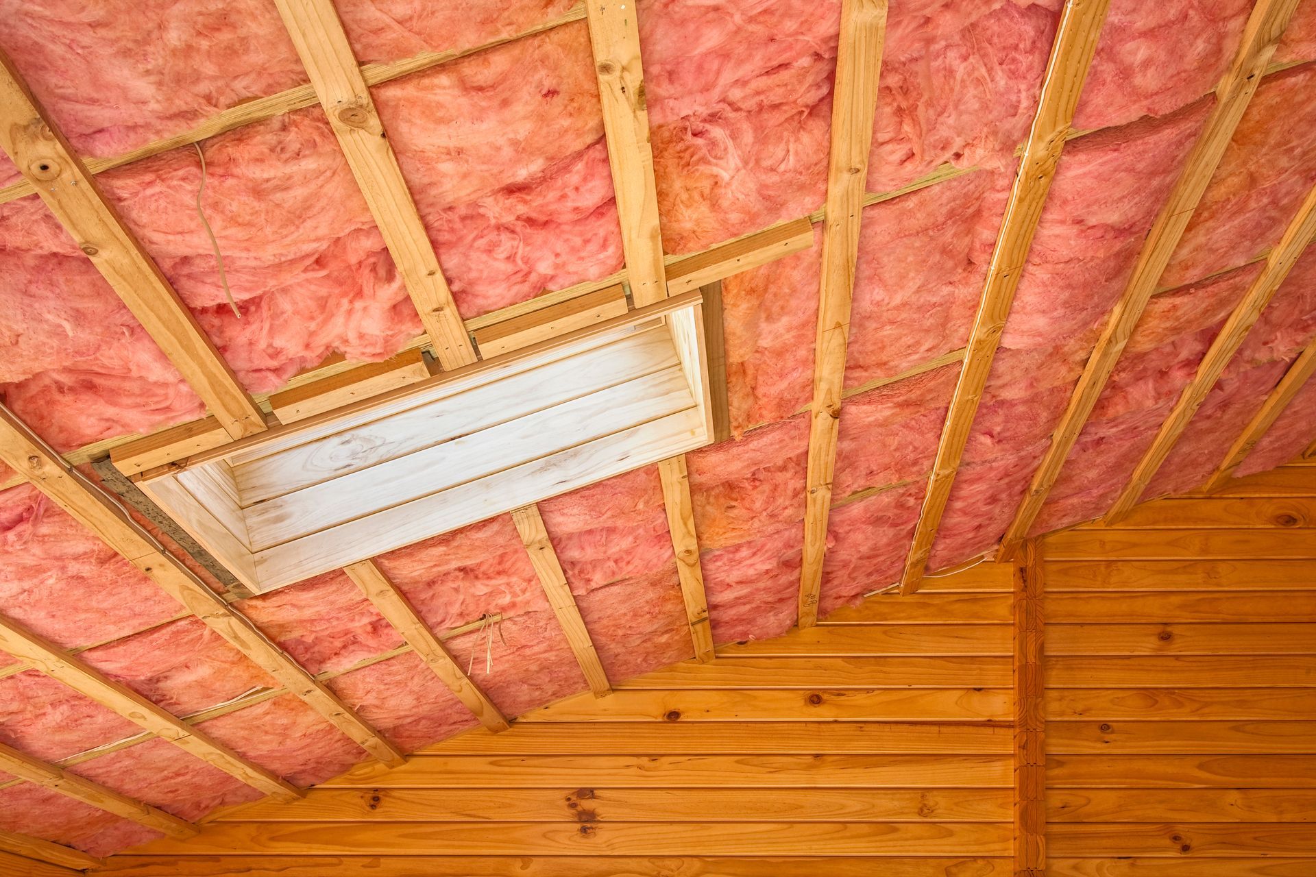Pink insulation in a wooden attic, framing a rectangular light fixture.