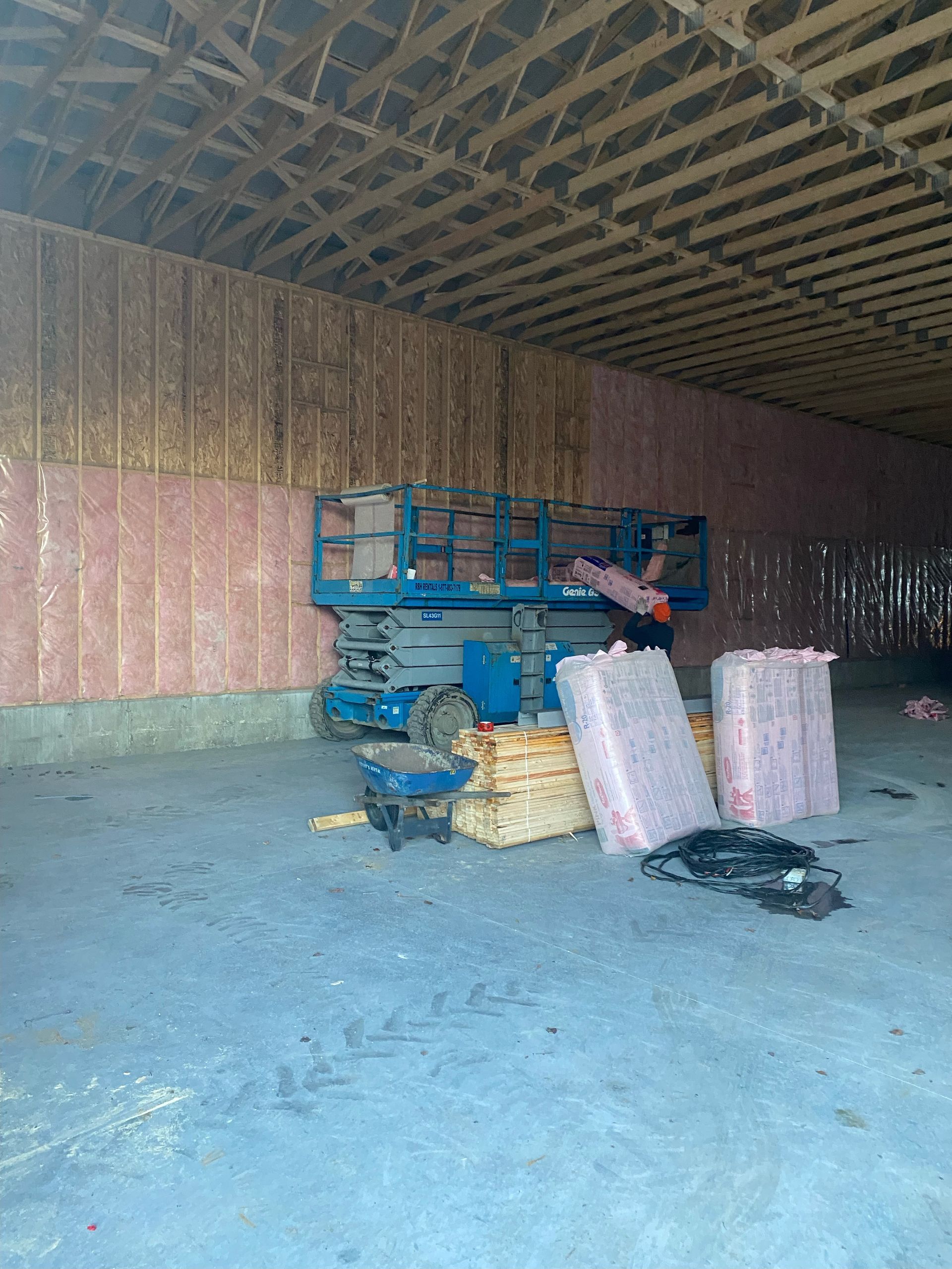 Interior of a building under construction with a blue lift, insulation, and wooden beams.