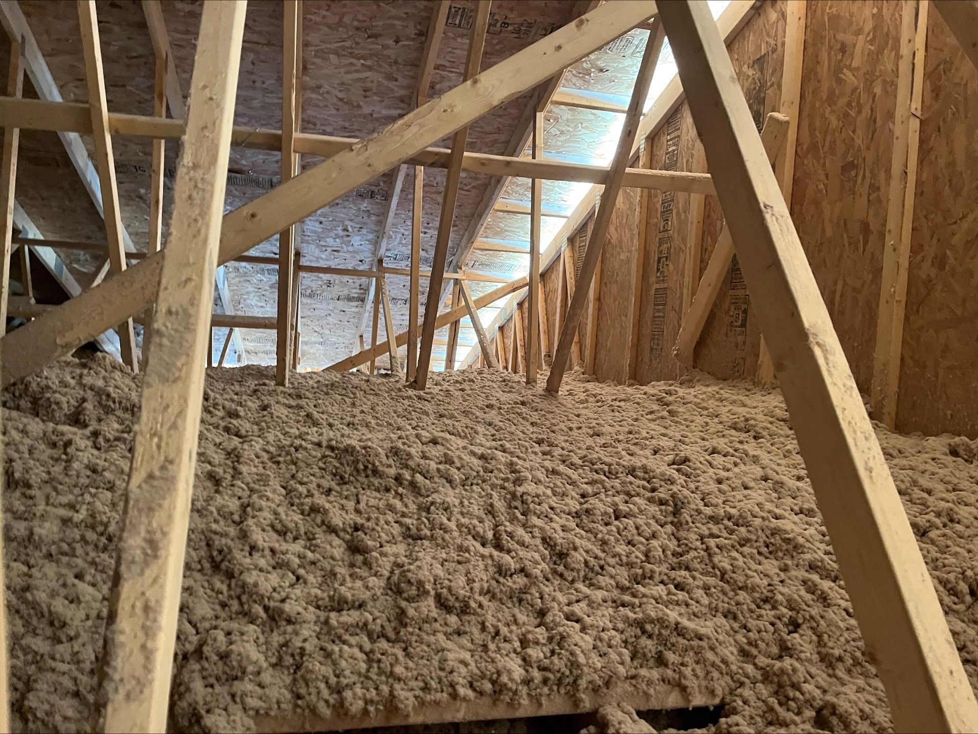 Attic filled with loose insulation, wooden rafters and beams.