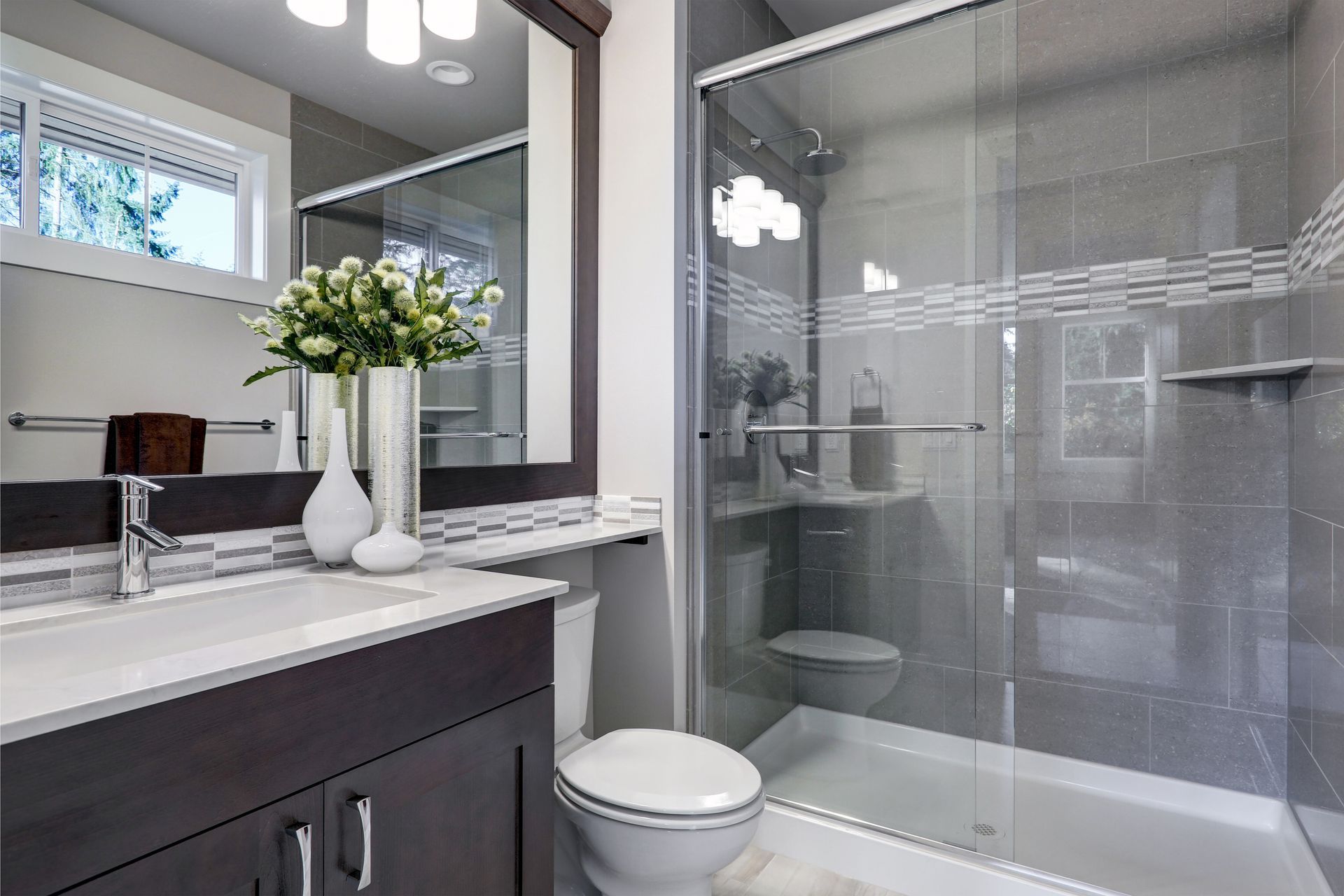 A modern bathroom with a glass shower, dark wood vanity, and decorative vases on the counter.