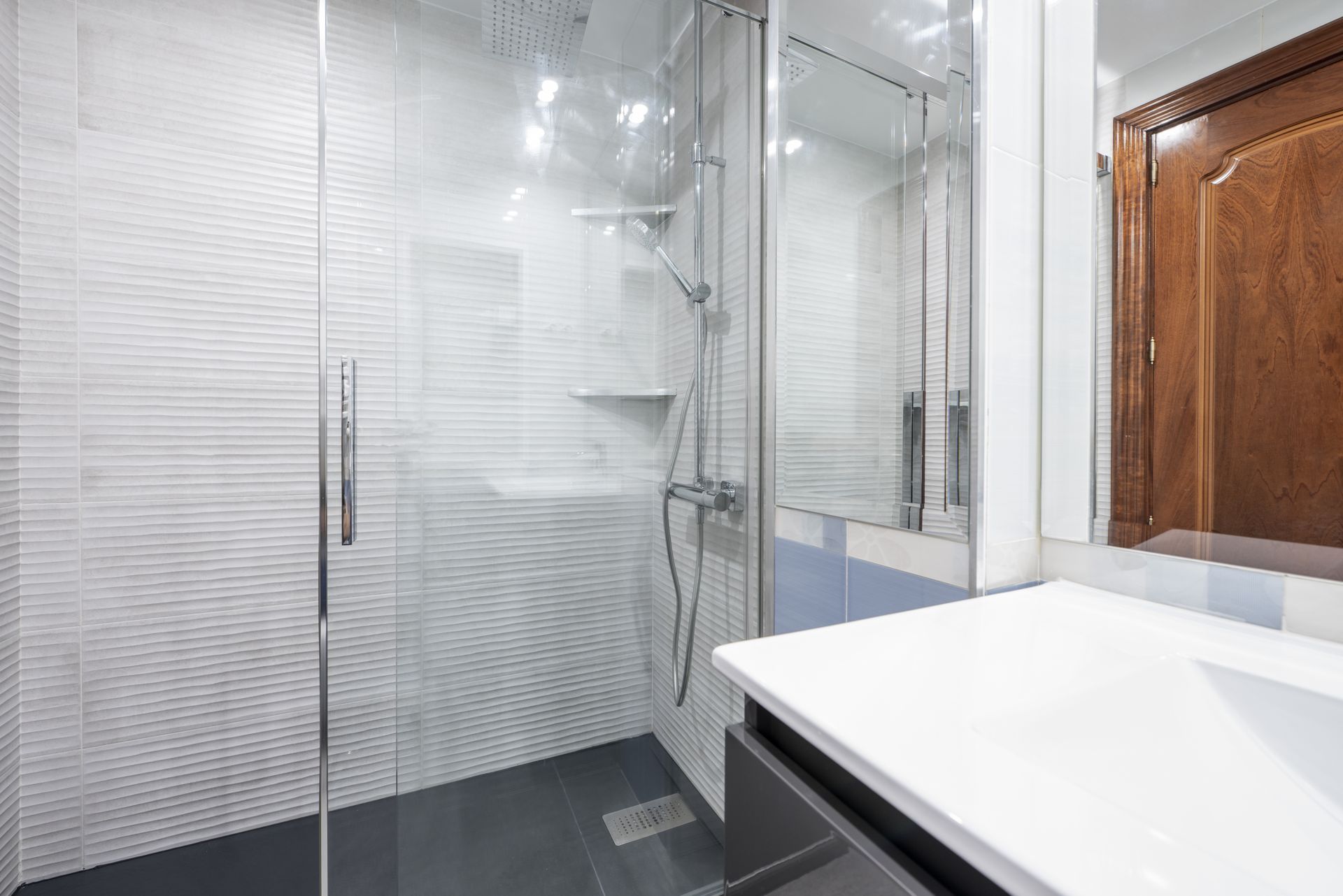 A modern walk-in shower with a frameless glass door, textured white tile walls, and chrome fixtures