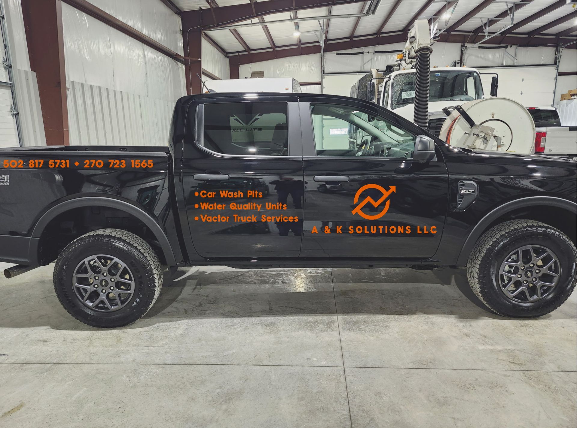 Three people inspecting a blue delivery truck with equipment. They are outside a modern building on a sunny day.