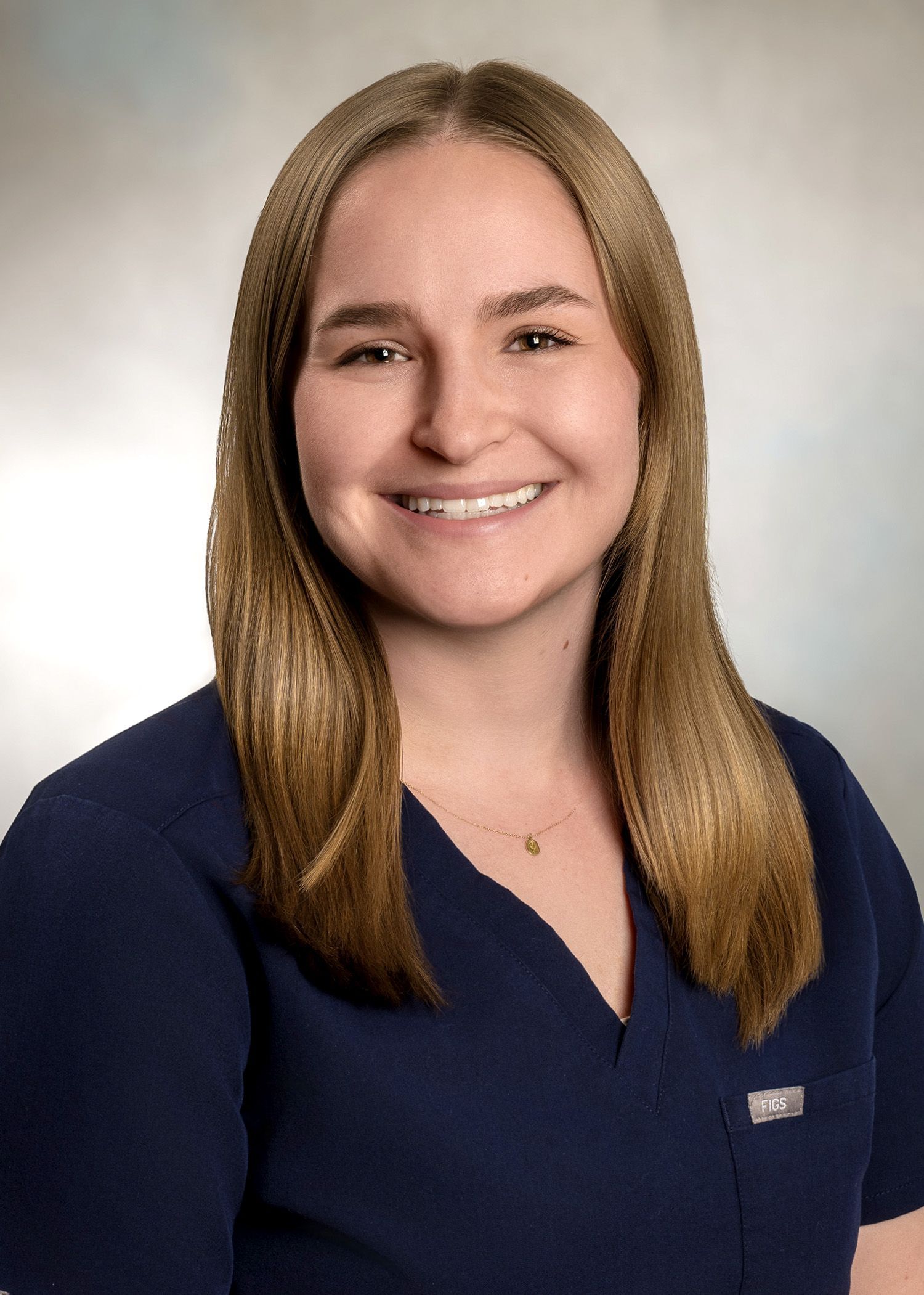 Woman with long blonde hair smiles, wearing a dark blue top, in a studio setting.