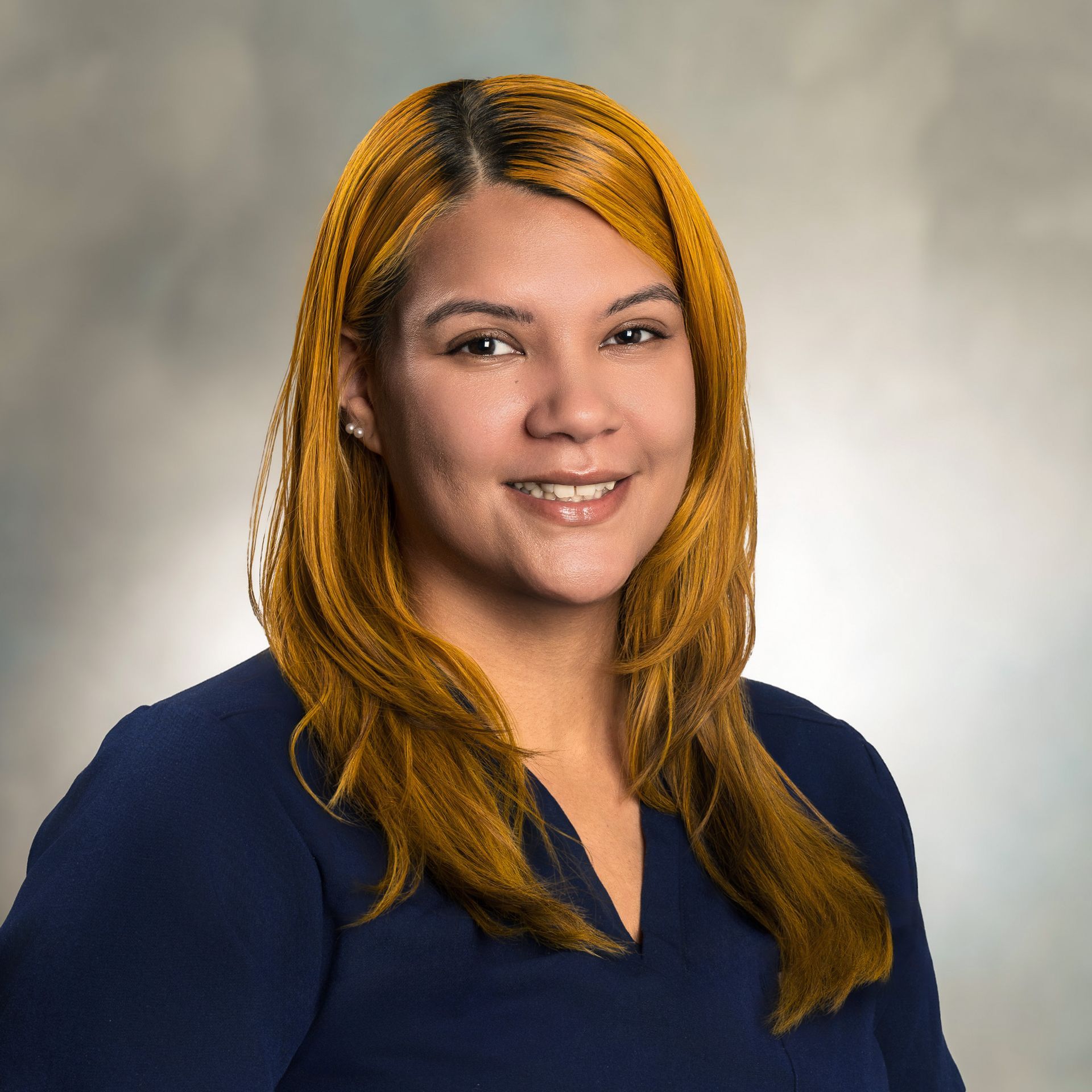 Woman with long, honey-blonde hair smiling, wearing a navy blue top, against a soft, blurred background.