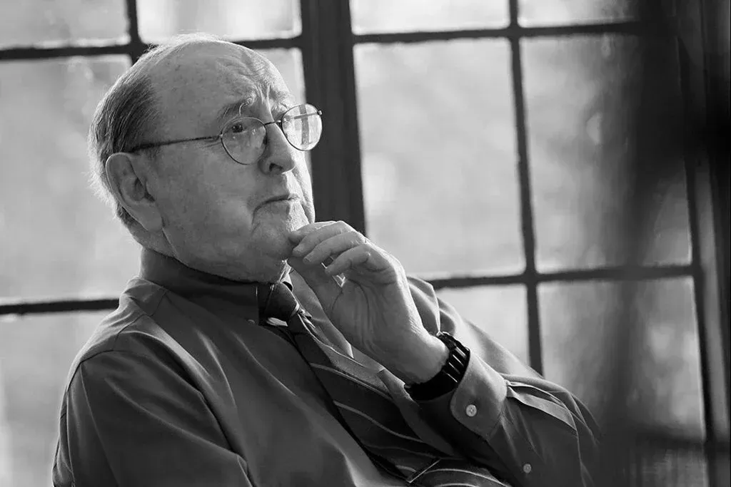 A man wearing glasses and a tie is sitting in front of a window.
