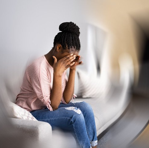 A woman is sitting on a couch covering her face with her hands.