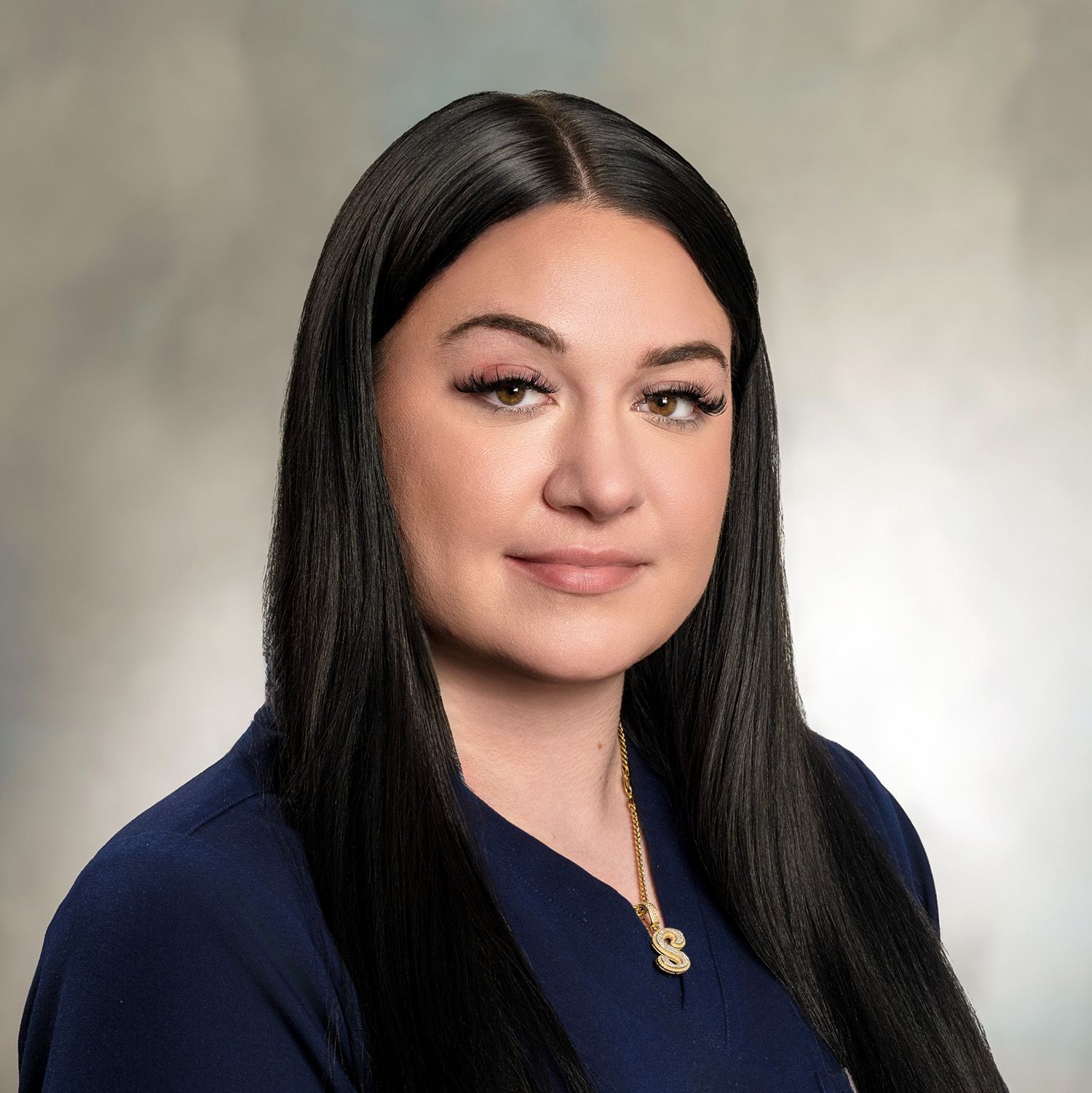 Woman with long dark hair, wearing a dark blue top, looking at the camera with a neutral expression.