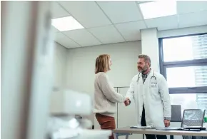 A doctor is shaking hands with a patient in a hospital room.