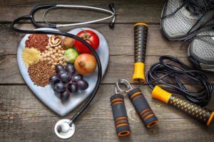 A heart shaped plate filled with fruits and vegetables next to a stethoscope and jumping rope.