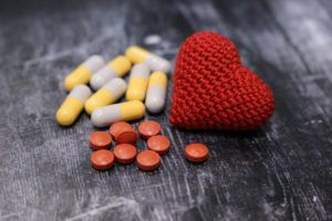 A knitted heart is sitting next to a pile of pills on a table.