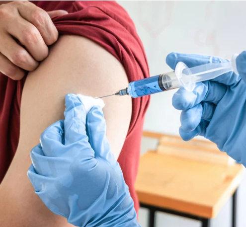 A person receiving an injection in the upper arm; blue liquid in the syringe, gloved hands.
