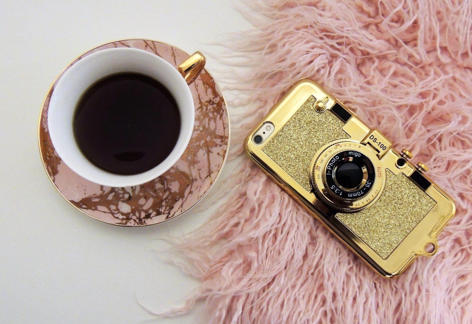 Op roze fluffy kleedje ligt een iphone met een kopje koffie ernaast
