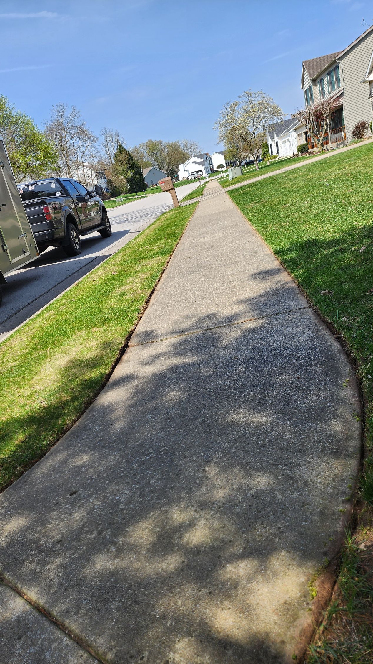 A sidewalk in a residential neighborhood with cars parked on the side of the road.