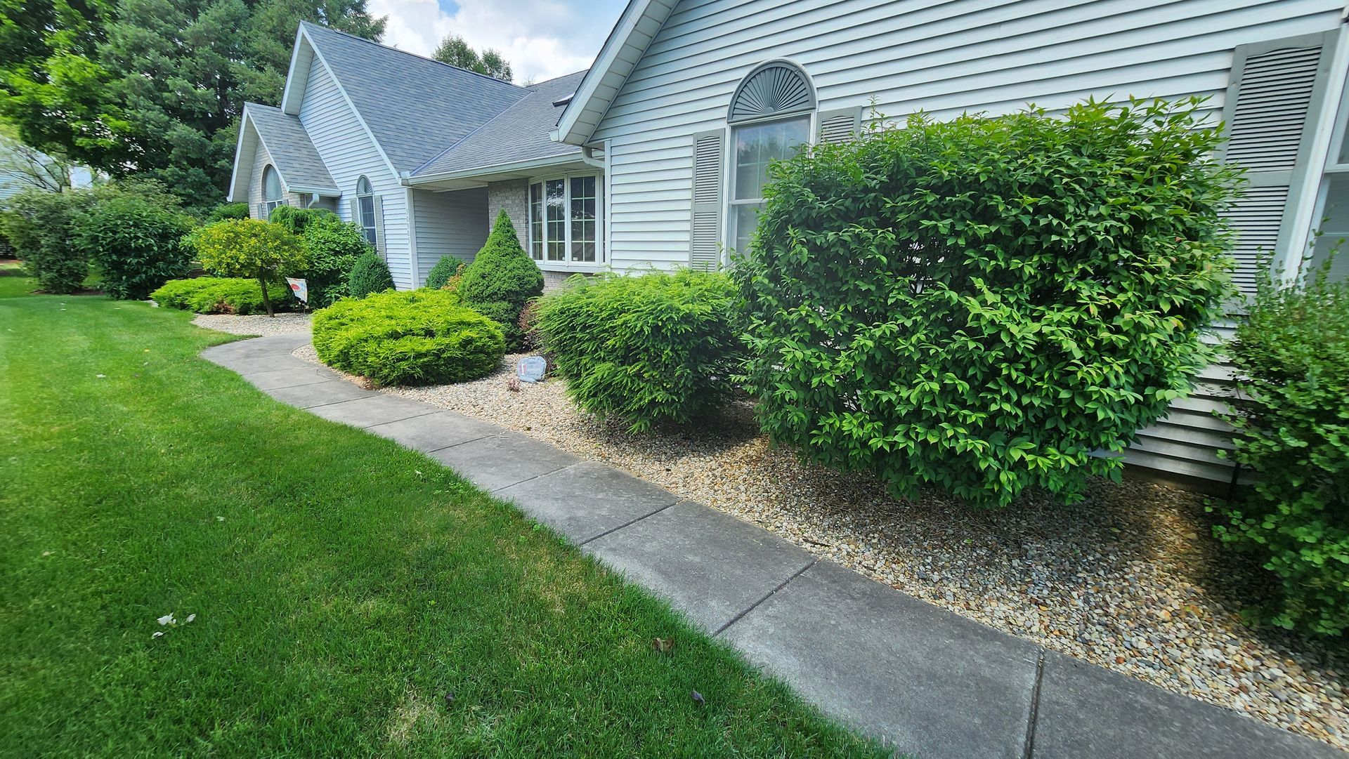 A white house with a lush green lawn and a sidewalk in front of it.