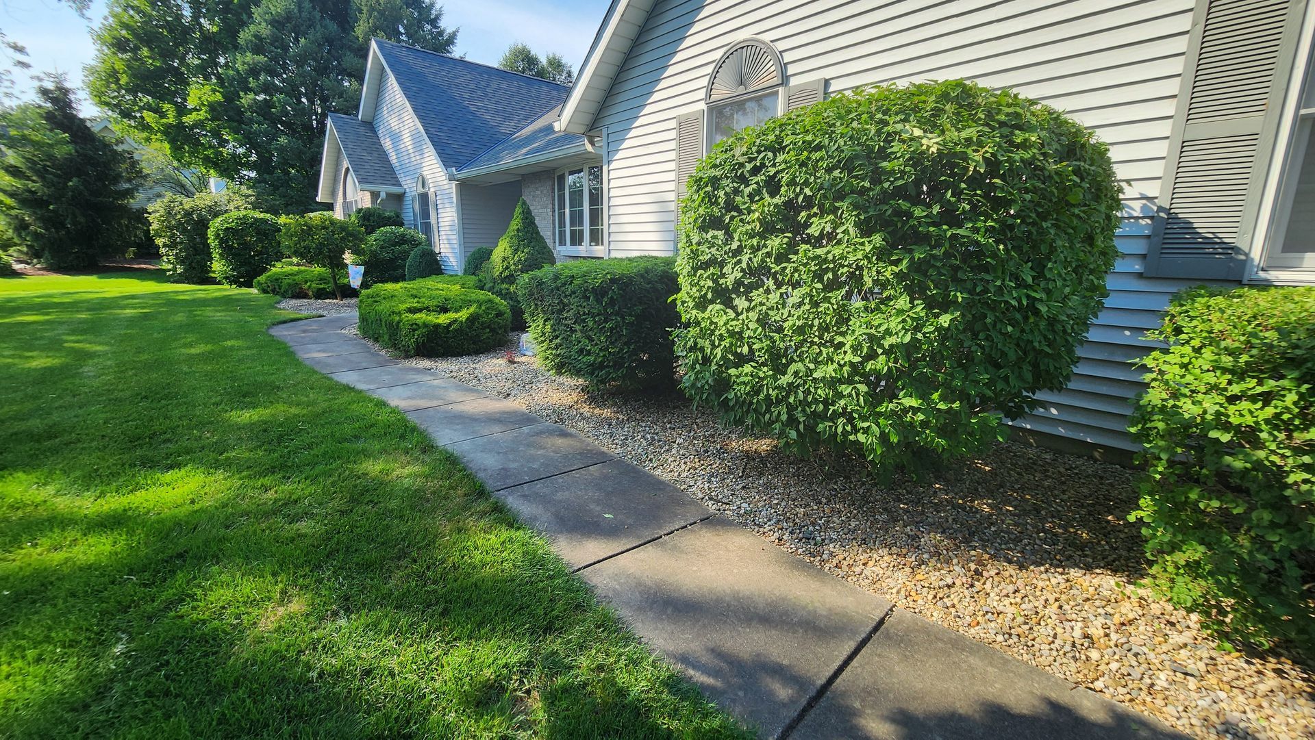 A sidewalk leading to a house with a lush green lawn and bushes.
