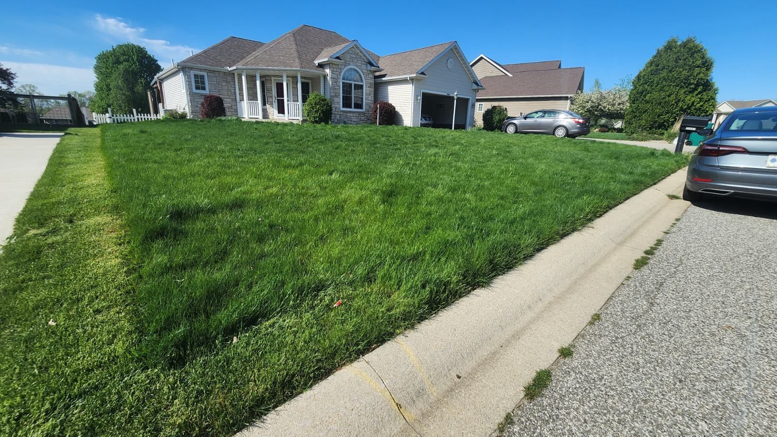 A car is parked in front of a house with a lush green lawn.
