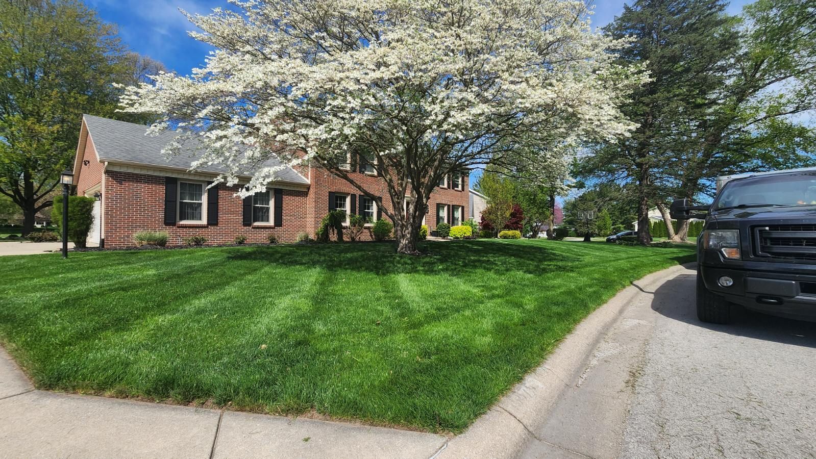 A black suv is parked in front of a brick house with a lush green lawn.