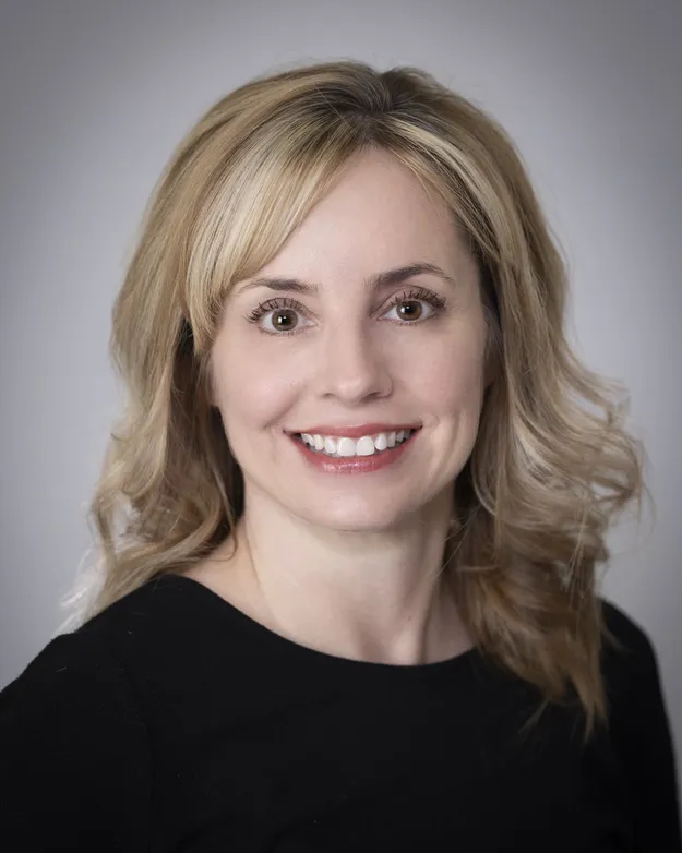 A woman with blonde hair and a black shirt is smiling for the camera.