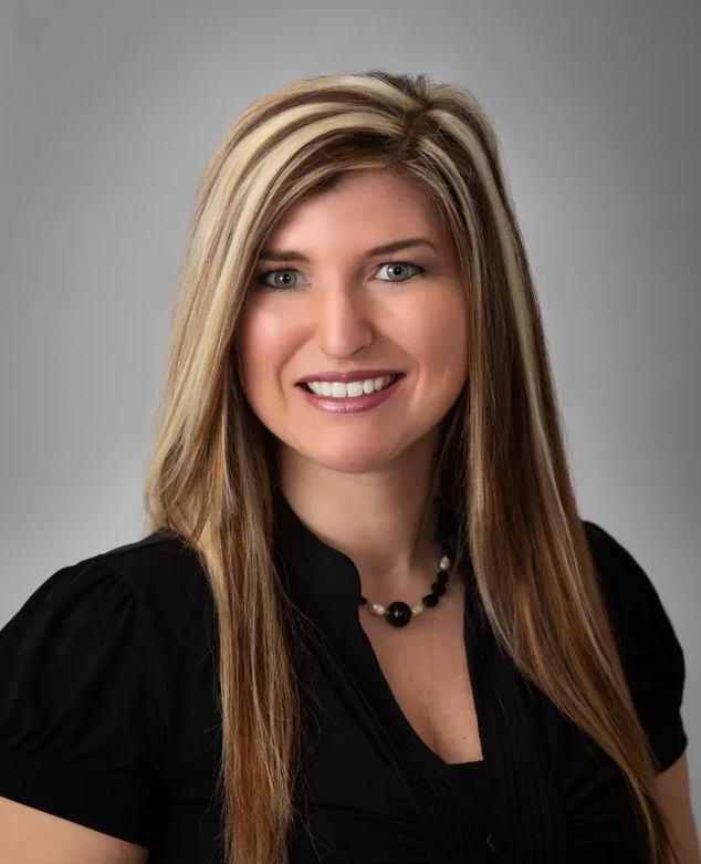 A woman with long blonde hair is wearing a black shirt and a black necklace