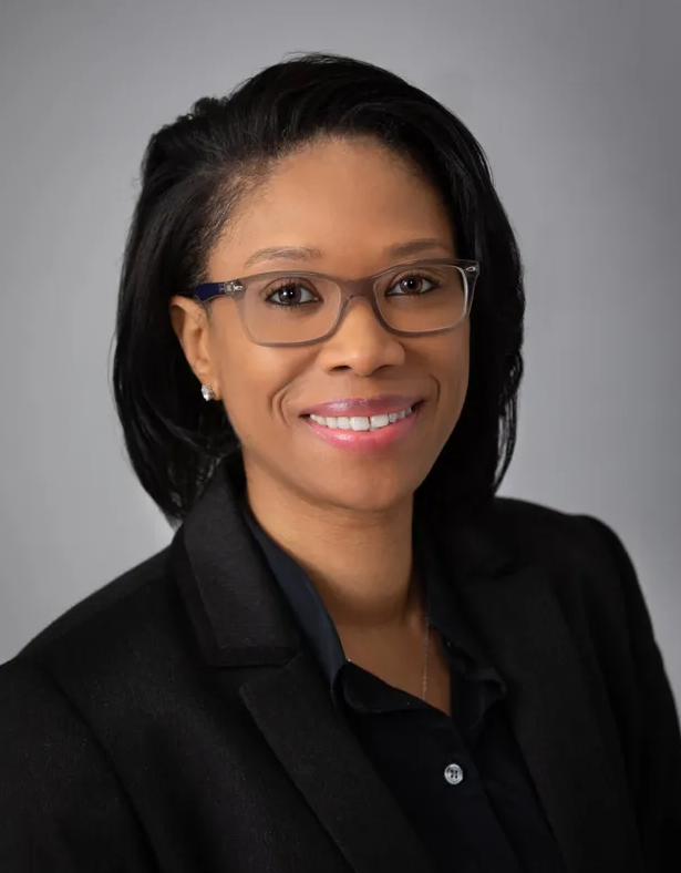 A woman wearing glasses and a black jacket is smiling for the camera.