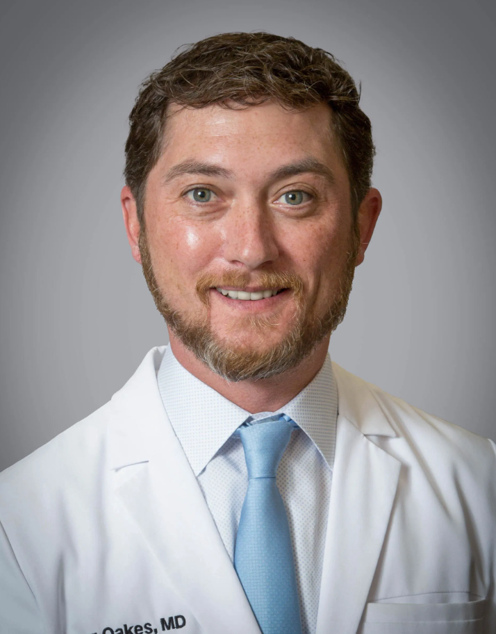 A man with a beard is wearing a white coat and blue tie.