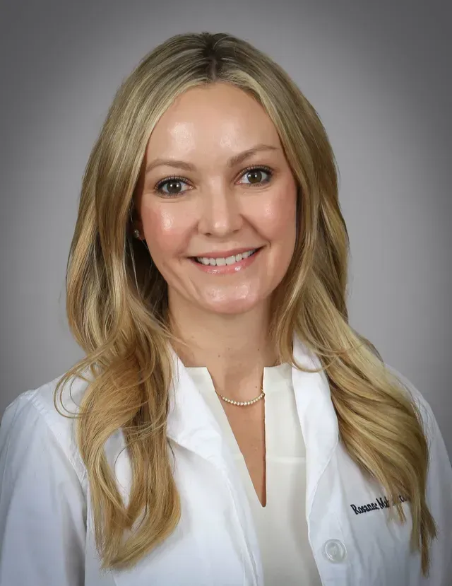 A woman in a white lab coat is smiling for the camera.