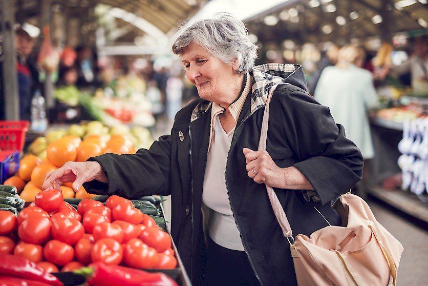 Older Woman at Vegetable Market Picking Up Tomato