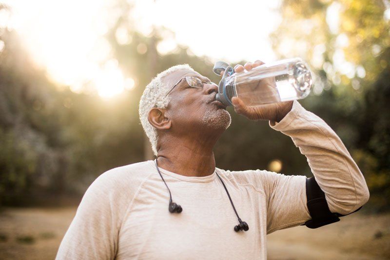 Older Man With Glasses and headphones drinking water during a workout