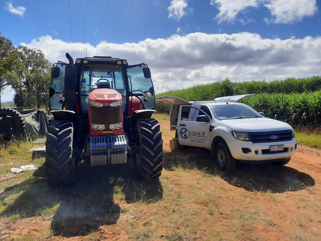 A Red Tractor is Parked Next to a White Truck in a Field — Giger Machinery Services in Bentley Park, QLD