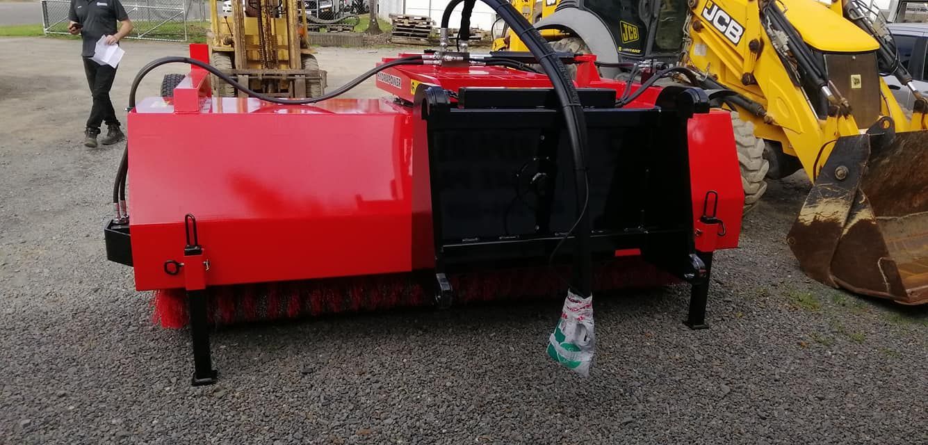 A Red and Black Broom is Parked in a Gravel Lot Next to a Yellow Excavator — Giger Machinery Services in Atherton, QLD