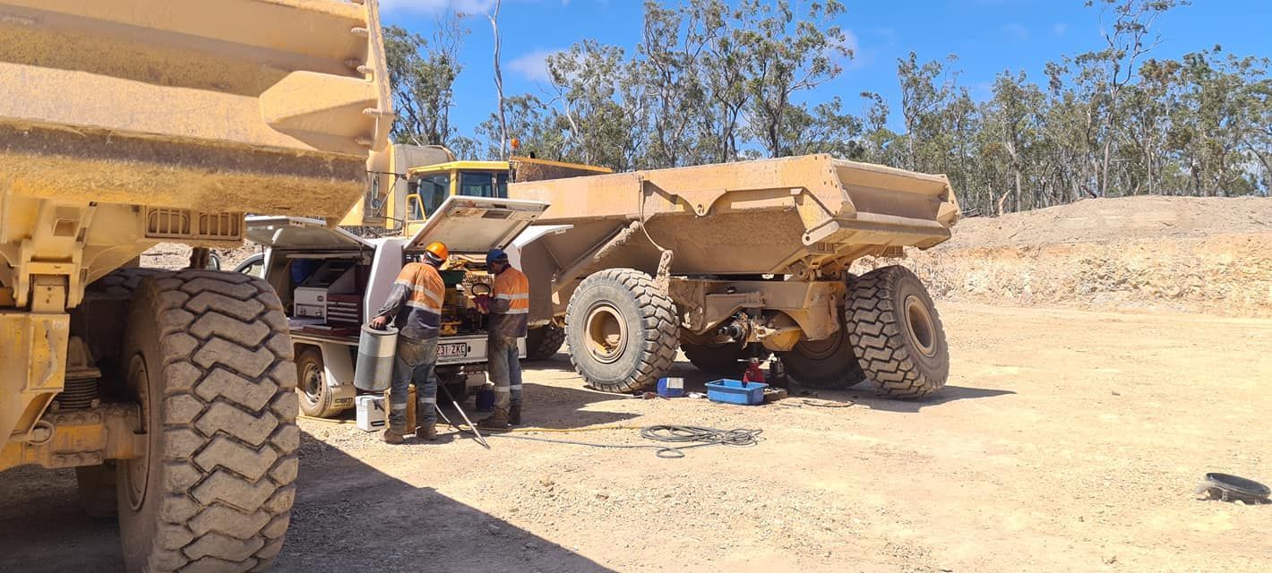 A Group of Men Are Working on a Dump Truck in a Dirt Field — Giger Machinery Services in Bentley Park, QLD